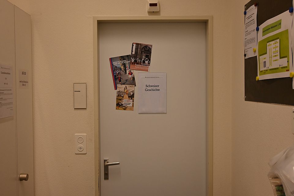 Neben dem Bibliotheksbüro befindet sich der Raum "Schweizergeschichte" mit der laufenden Signatur SC. Im Eingangsbereich wqeisen rote Pinnwände auf die Benutzung und den Aufbau der Bibliothek hin.