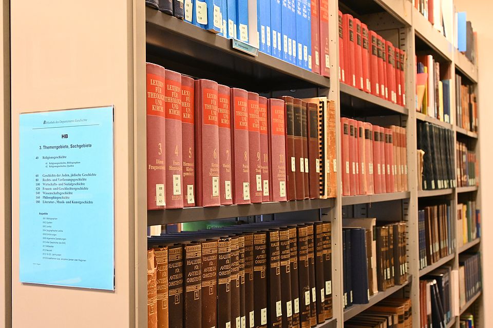 Im Lesesaal hinten rechts befindet sich der Bibliotheksraum "Handbuch". Dort finden sich Nachschlagewerke, Einführungen und Enzyklopädien thematisch gegliedert unter der Signatur HB. Diese tragen blaue Signaturschilder und sind von der Ausleihe ausgenommen.